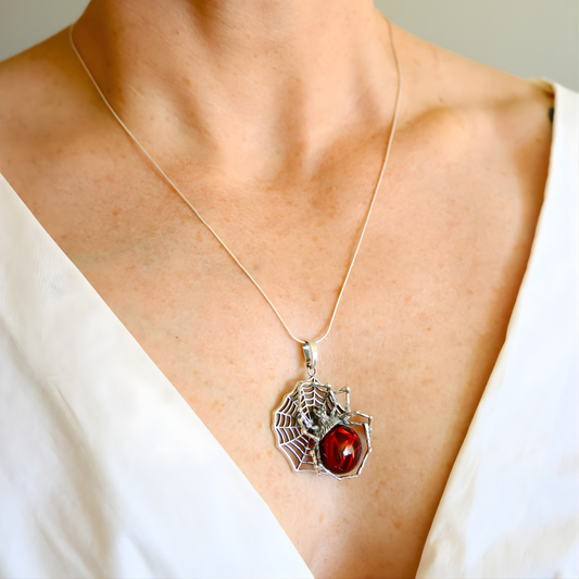 amber Necklace with a spider web and red gemstone pendant on a person wearing a white top.
