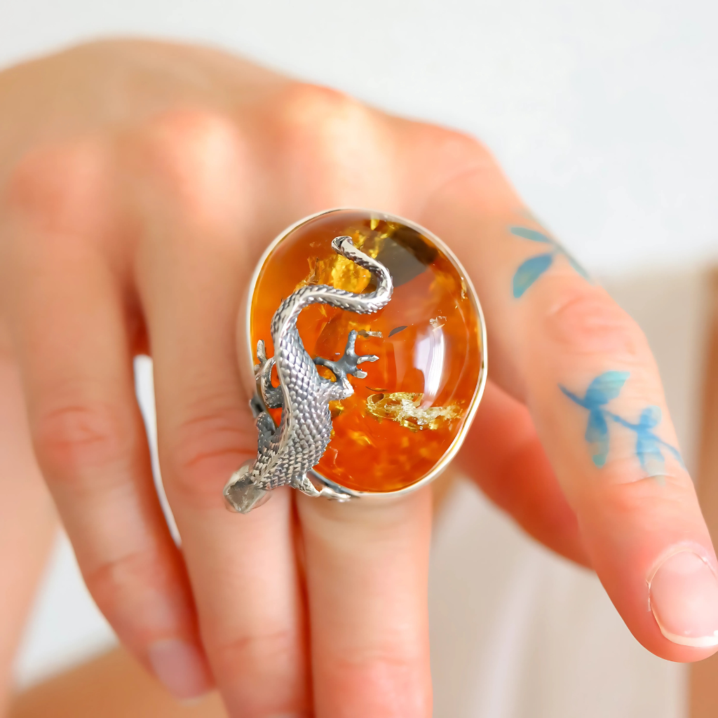 Statement ring with a silver lizard design on an orange background worn on a finger.