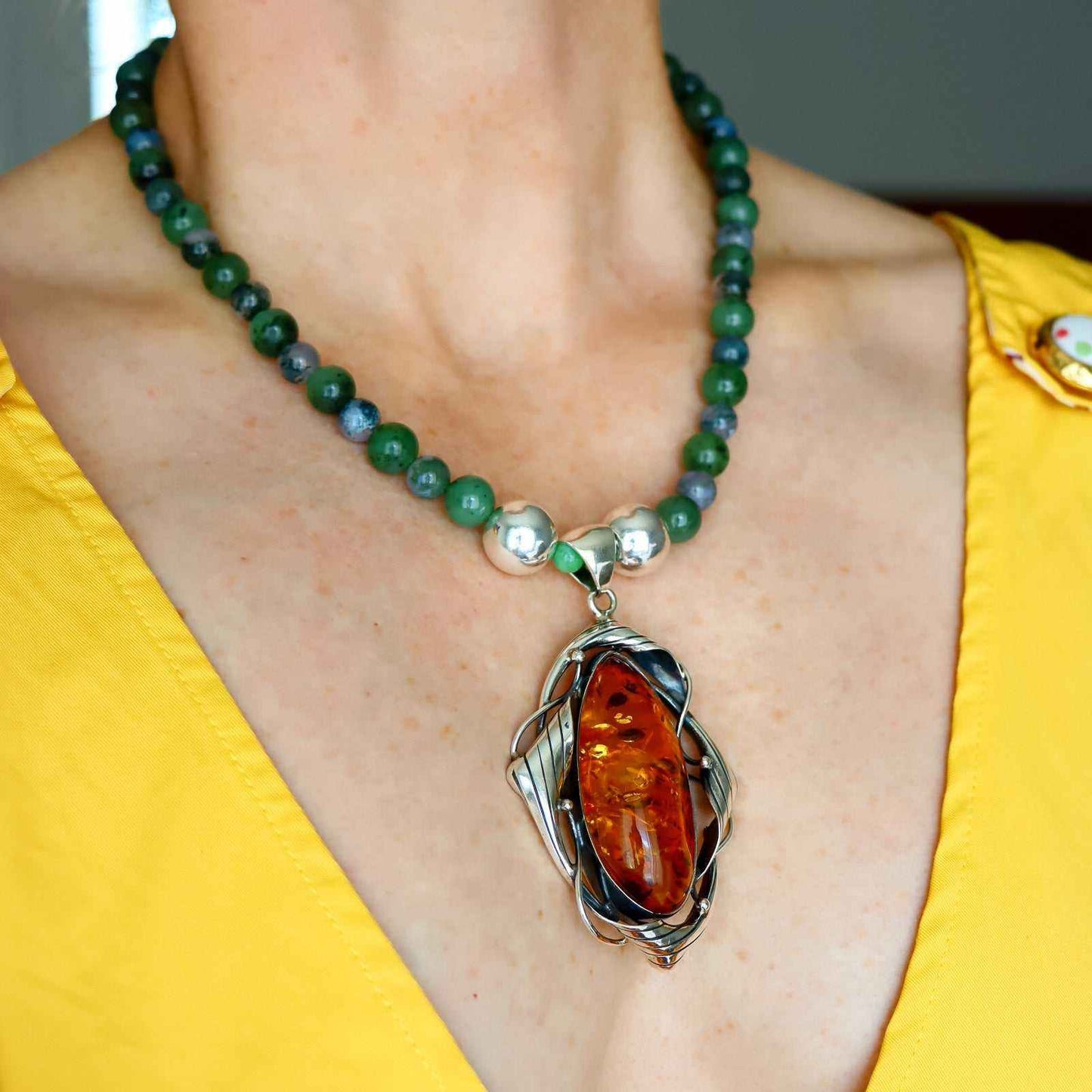 Cognac amber statement necklace with Canadian jade, green moss agate beads, and sterling silver pendant worn on model.
