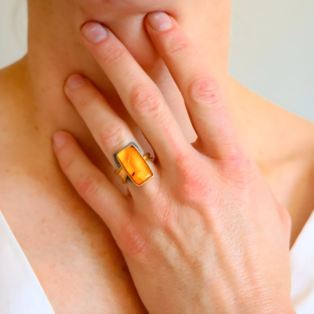 Close-up of a hand wearing a amber ring with a yellow gemstone on a neutral background