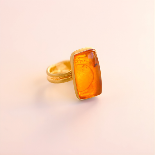 Gold amber ring with a rectangular amber stone on a light pink background
