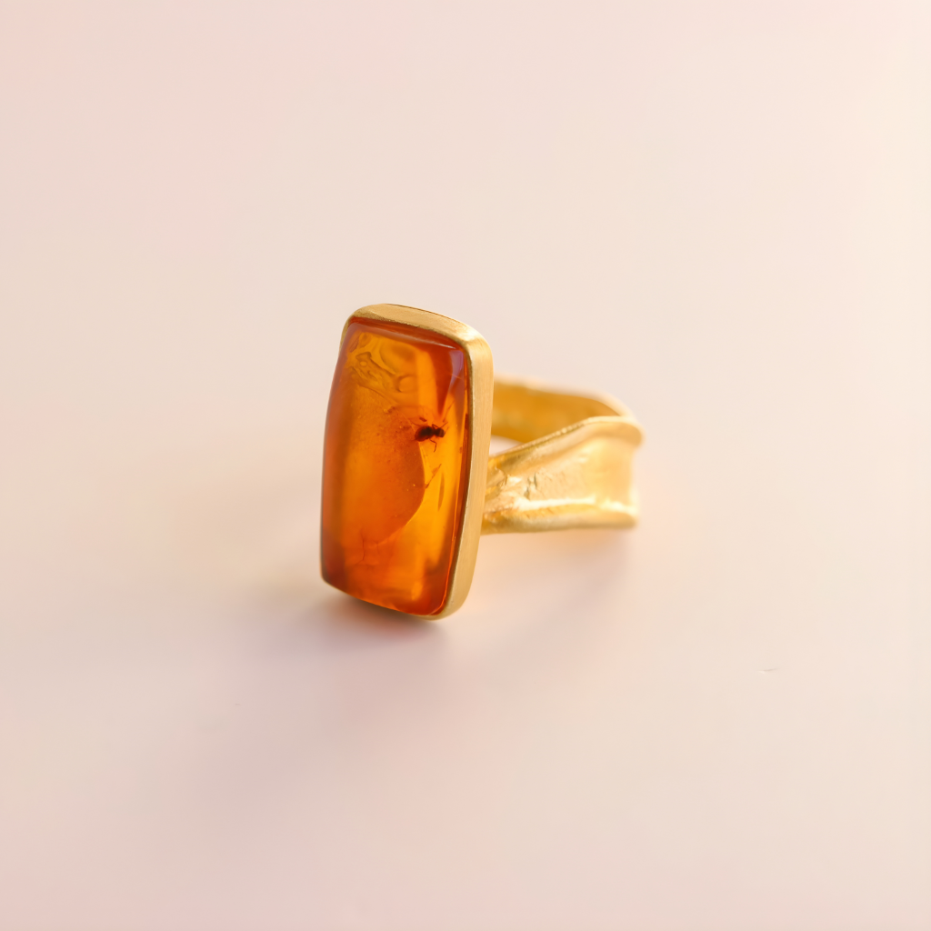 Gold amber ring with amber stone on a beige background