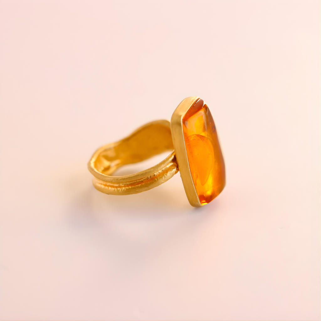 Gold amber ring with a large amber stone on a light pink background