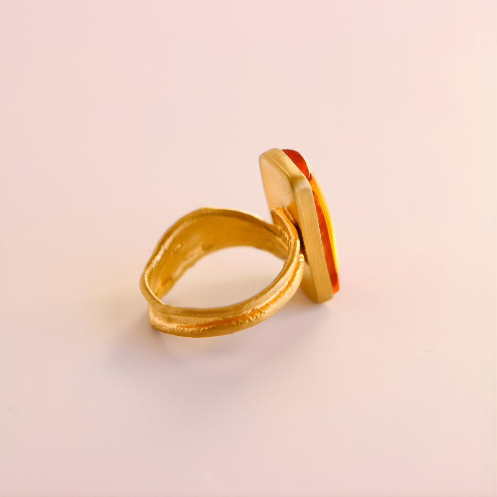 Gold amber ring with a red stone on a light pink background