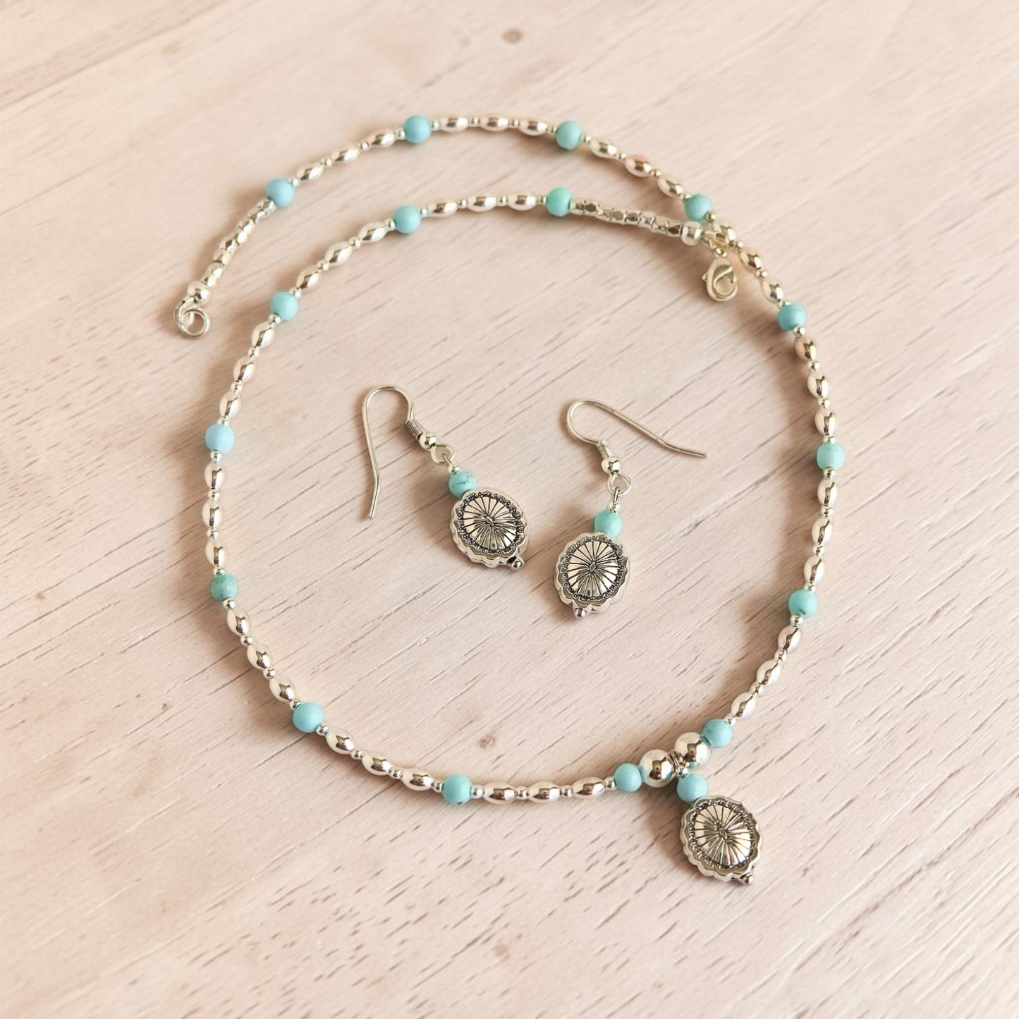turquoise beaded necklace with silver accents and silver earrings on gray white background