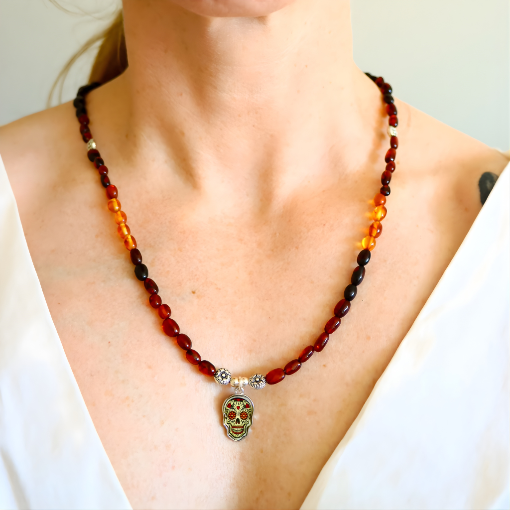 Baltic amber beaded necklace worn on model featuring cherry, cognac, and butterscotch amber beads with a Day of the Dead skull charm.
