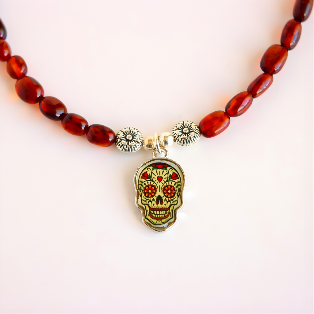 Close-up of Day of the Dead skull pendant on amber beaded necklace with silver flower spacer beads.