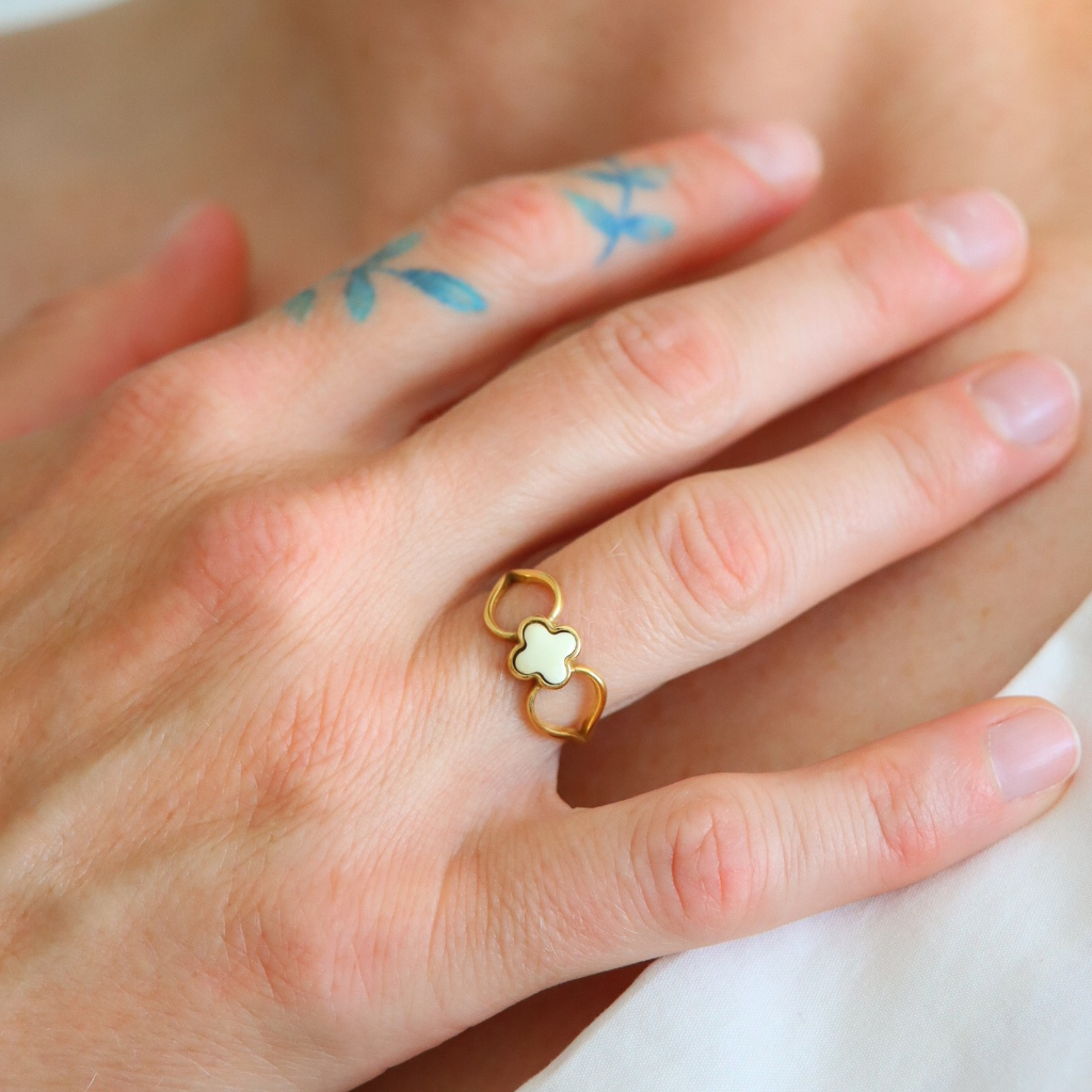 Hand wearing a gold amber ring with a four leaf clover design on a blurred background