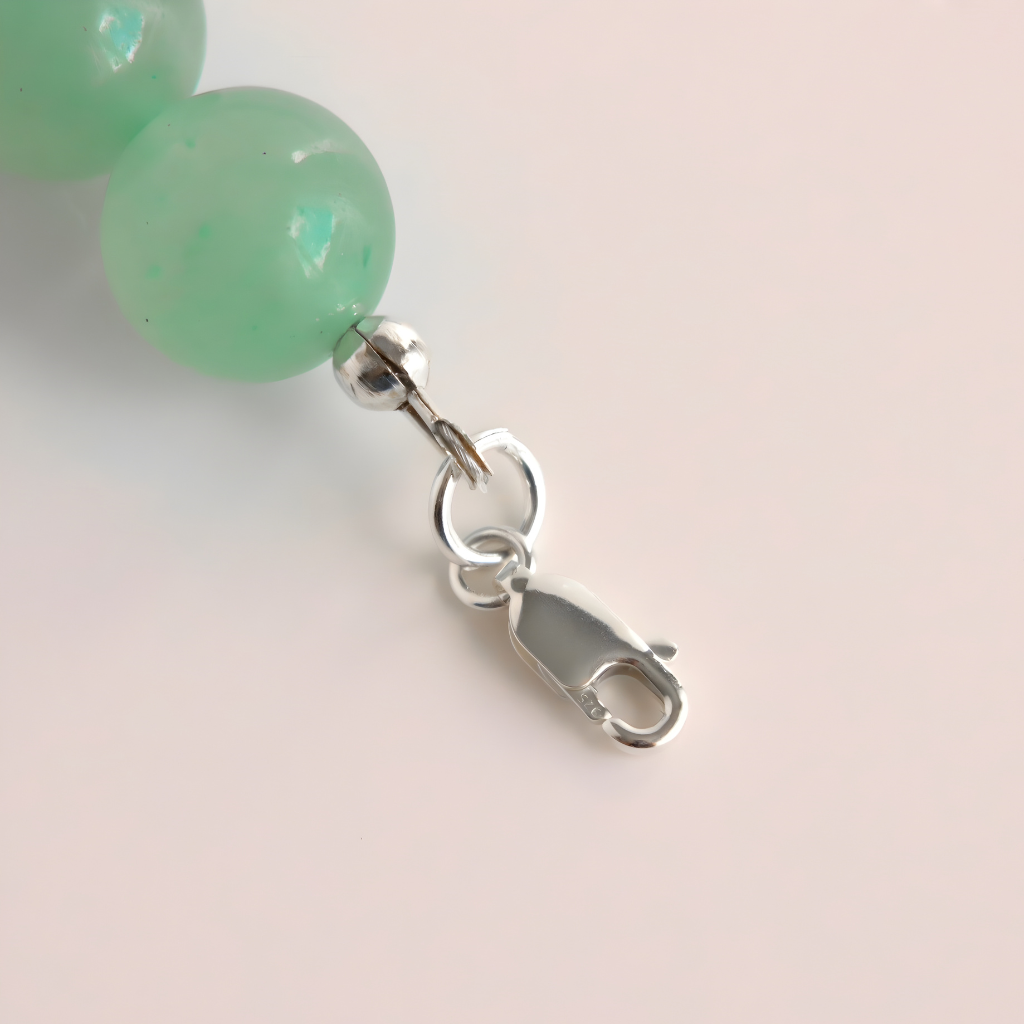 Close-up of green beads with a silver clasp on a light pink background