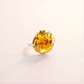 Gold flower ring with a large yellow gemstone on a light beige background