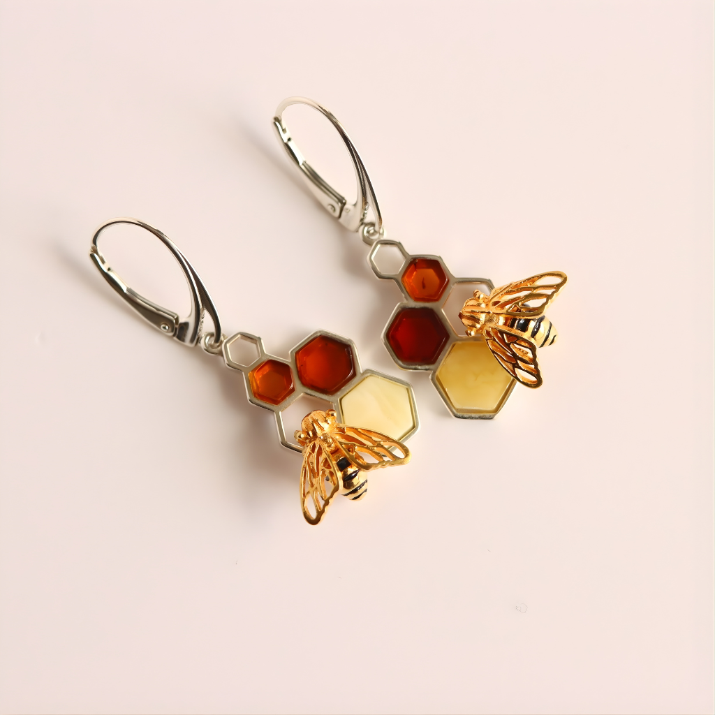 Pair of amber earrings with honeycomb and bee designs on a light pink background