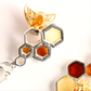 Close-up of a gold and silver honeycomb amber earrings with a bee on a white background
