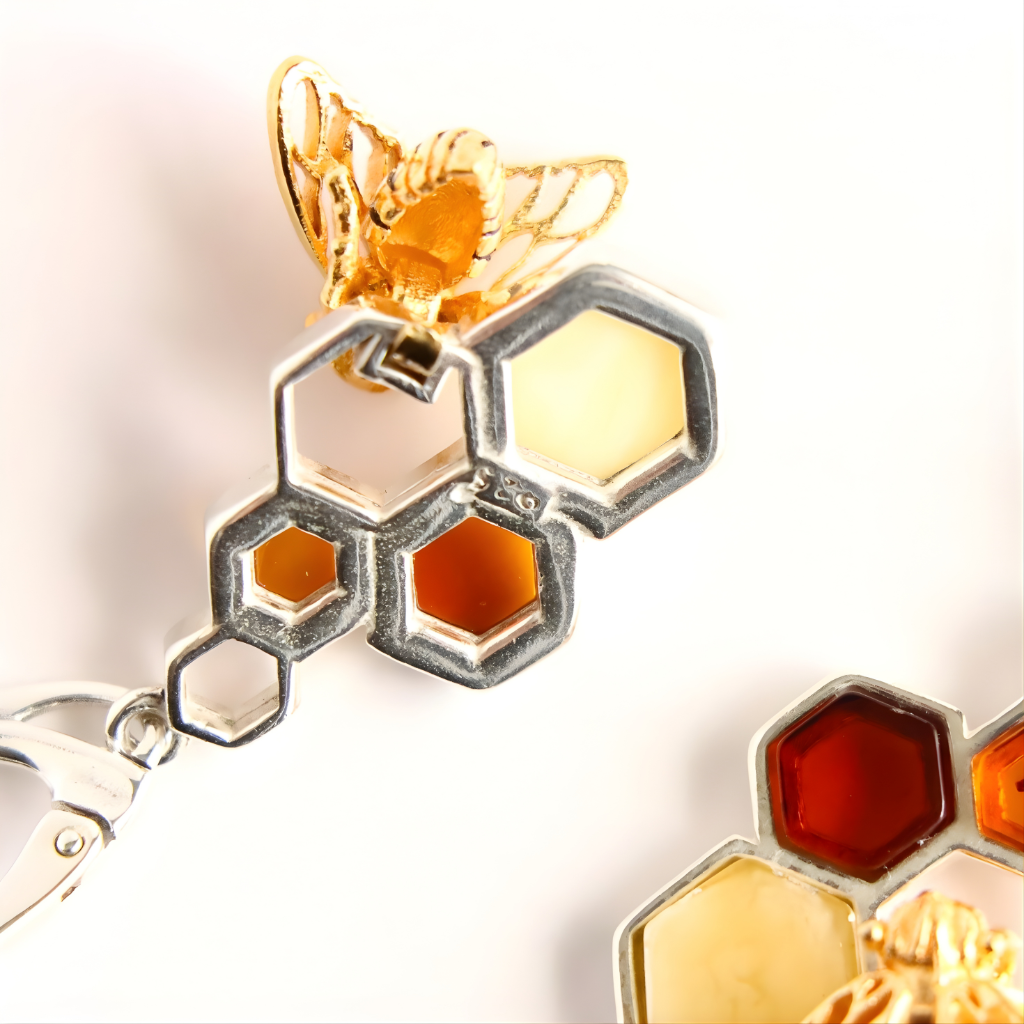 Close-up of a gold and silver honeycomb amber earrings with a bee on a white background