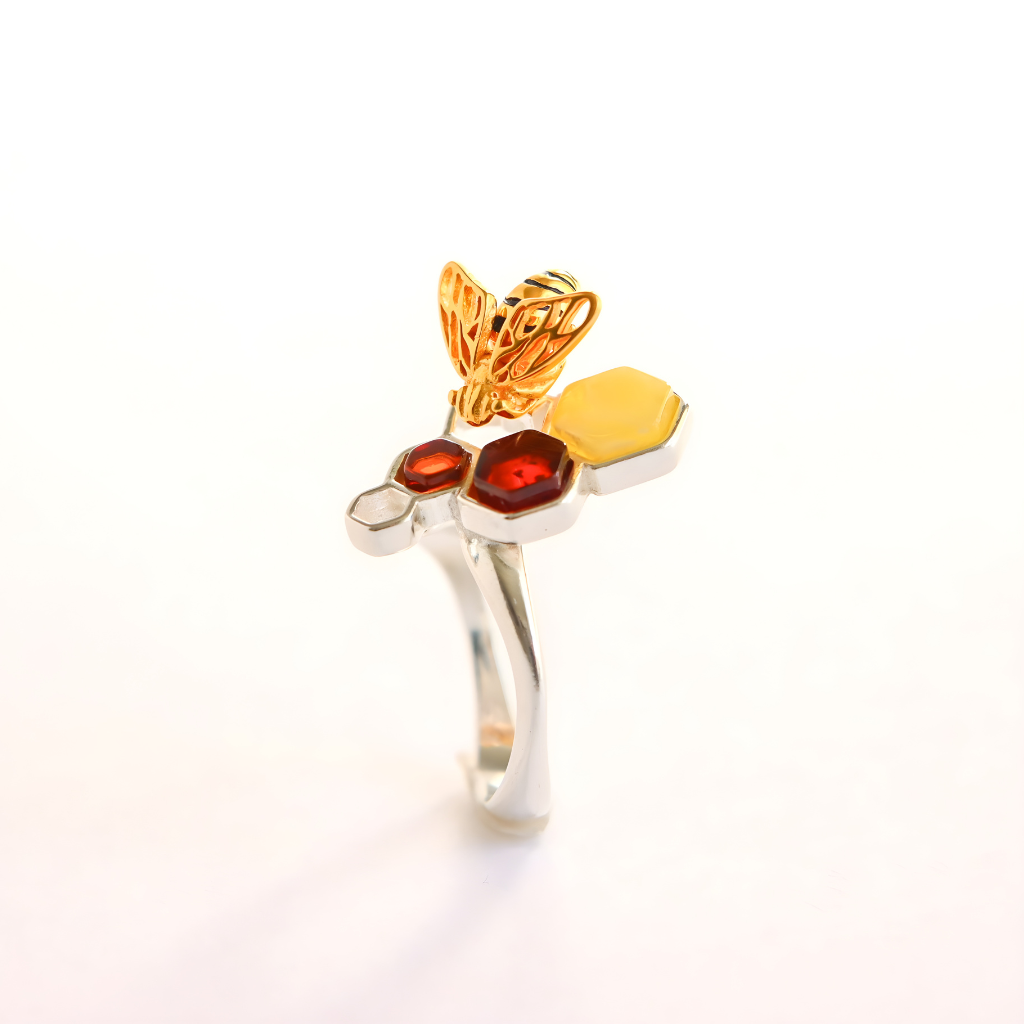Gold and silver amber ring with a butterfly and red gemstone on a white background