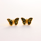Butterfly-shaped amber earrings with gold frame and green gemstones on a white background