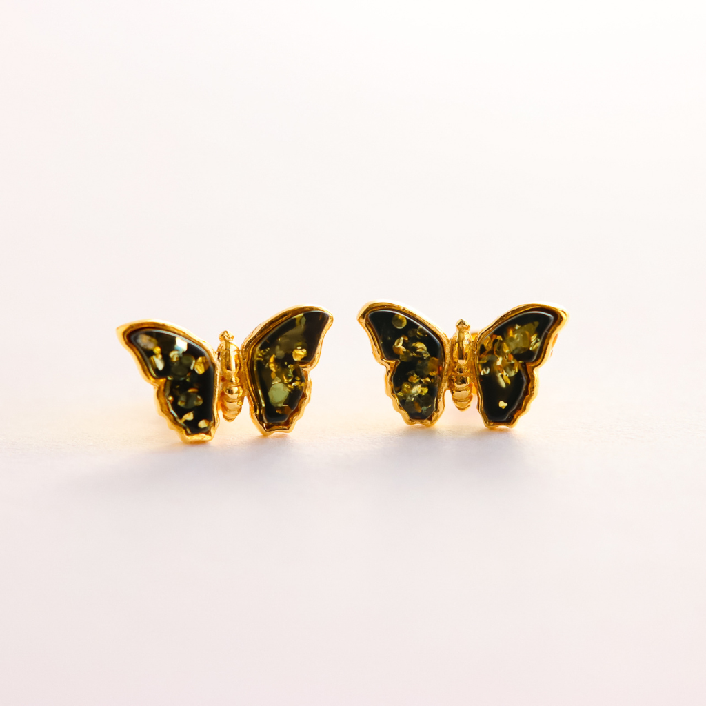 Butterfly-shaped amber earrings with gold frame and green gemstones on a white background