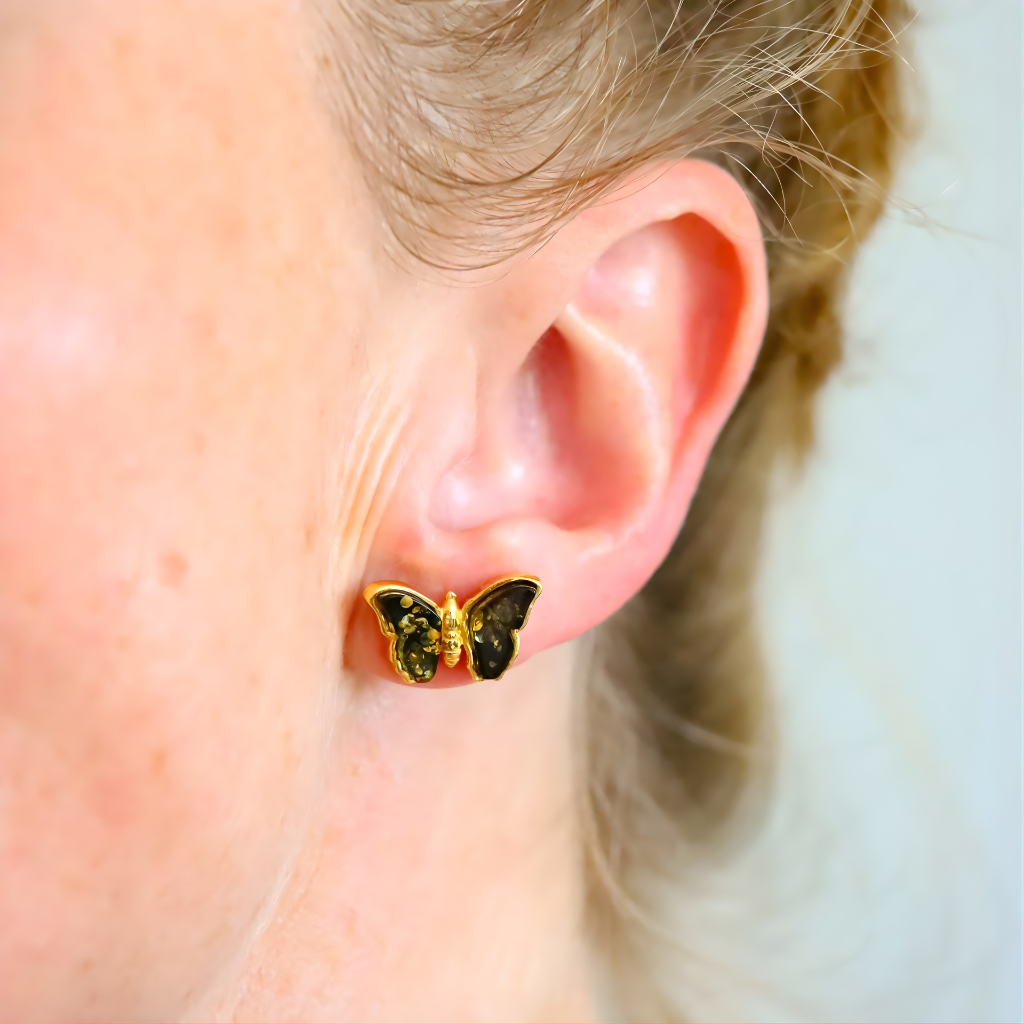Close-up of an ear wearing a gold butterfly amber earrings with green gemstones.