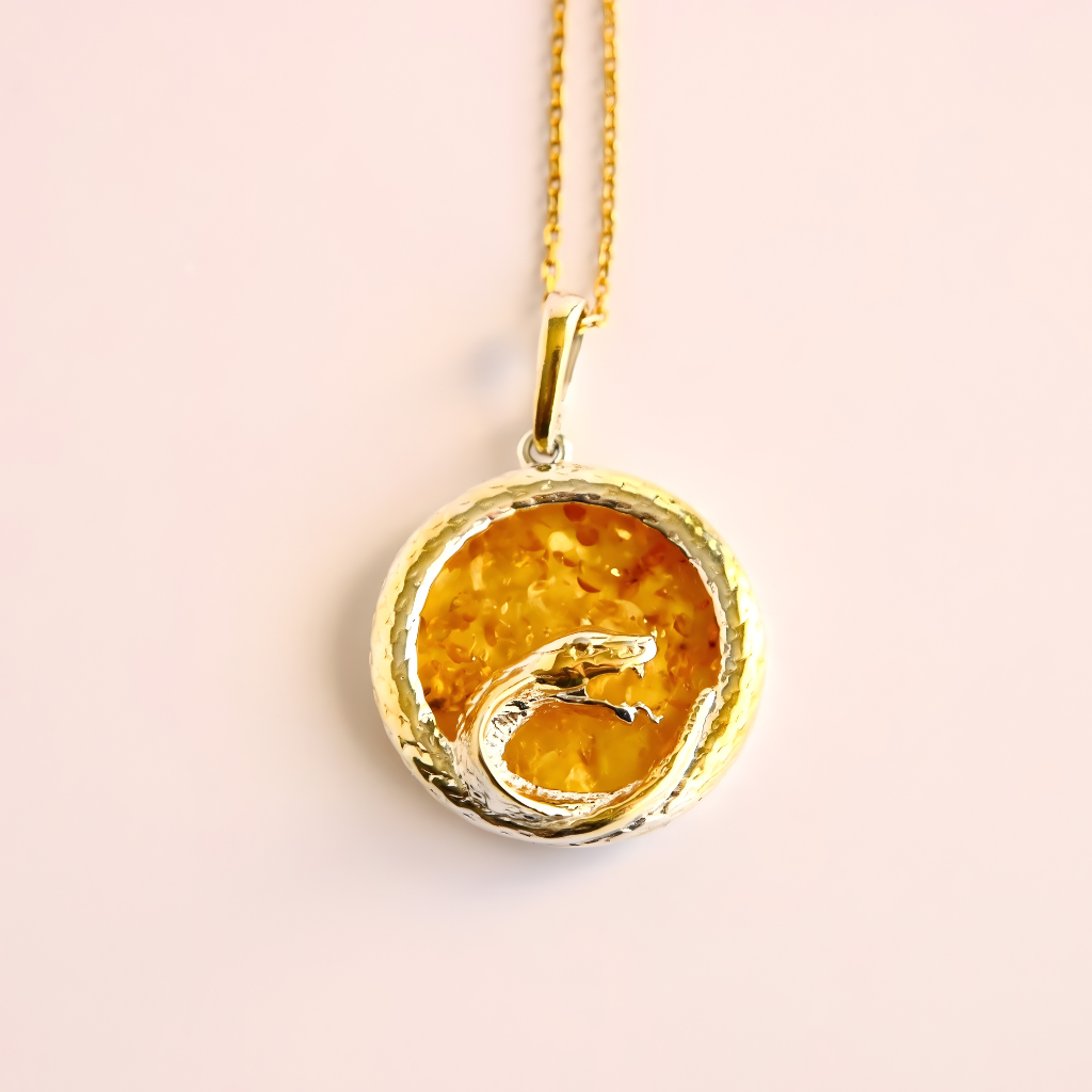 Gold pendant amber necklace with a yellow stone on a light pink background