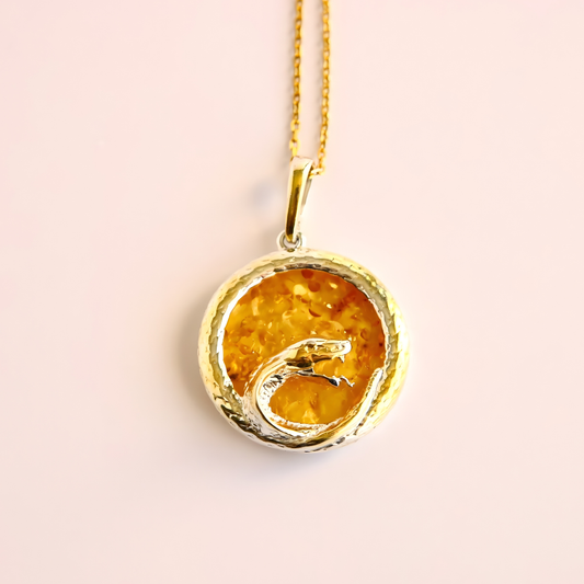 Gold pendant amber necklace with a yellow stone on a light pink background