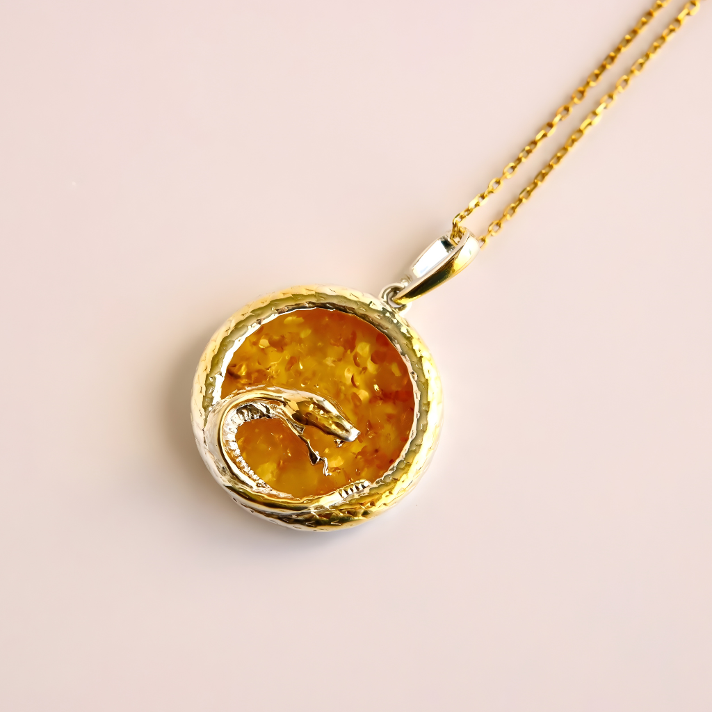 Gold amber necklace with a round pendant featuring a snake design on a light pink background