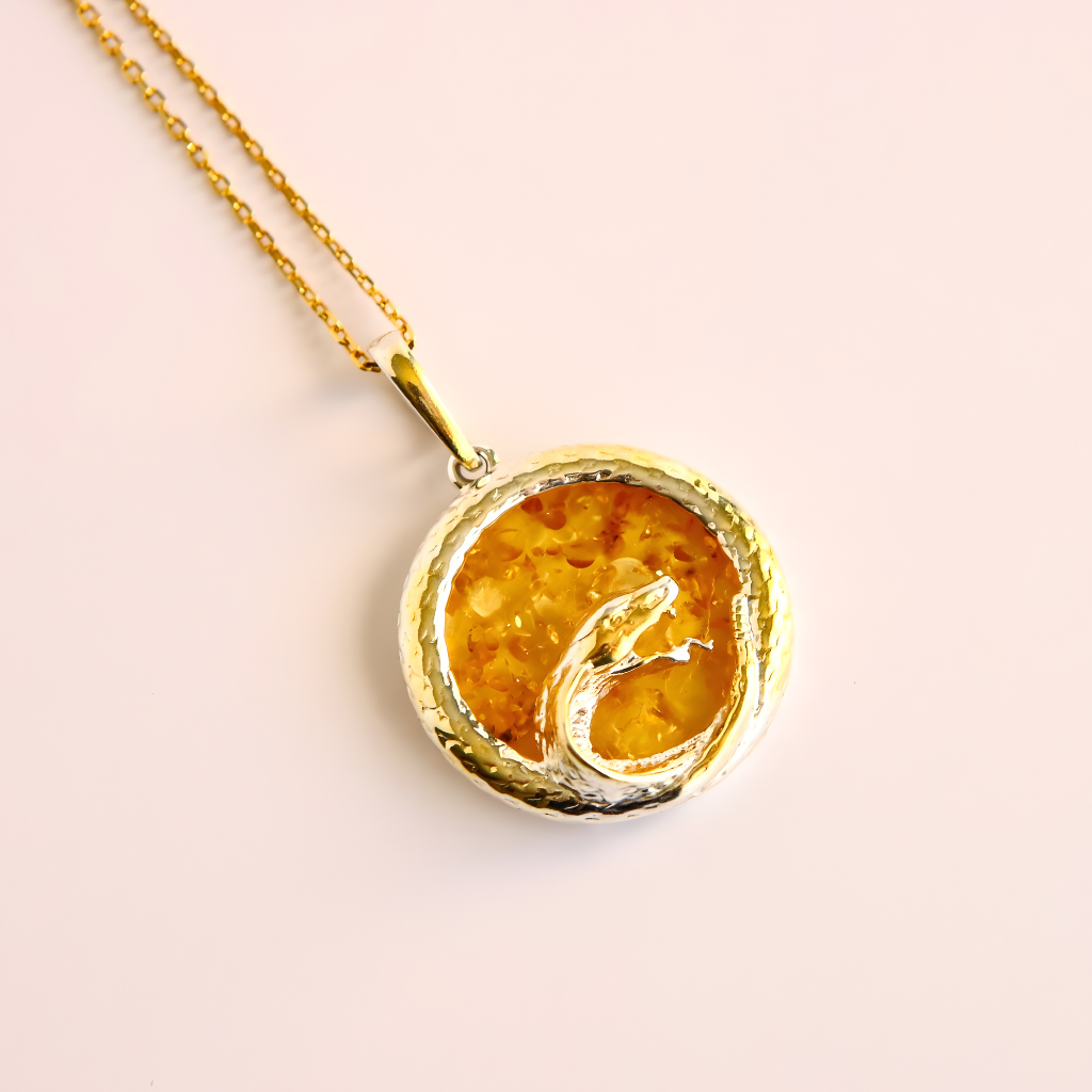 Gold amber necklace with a round pendant featuring a snake design on a light pink background