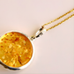 Gold amber necklace with a round pendant on a light pink background