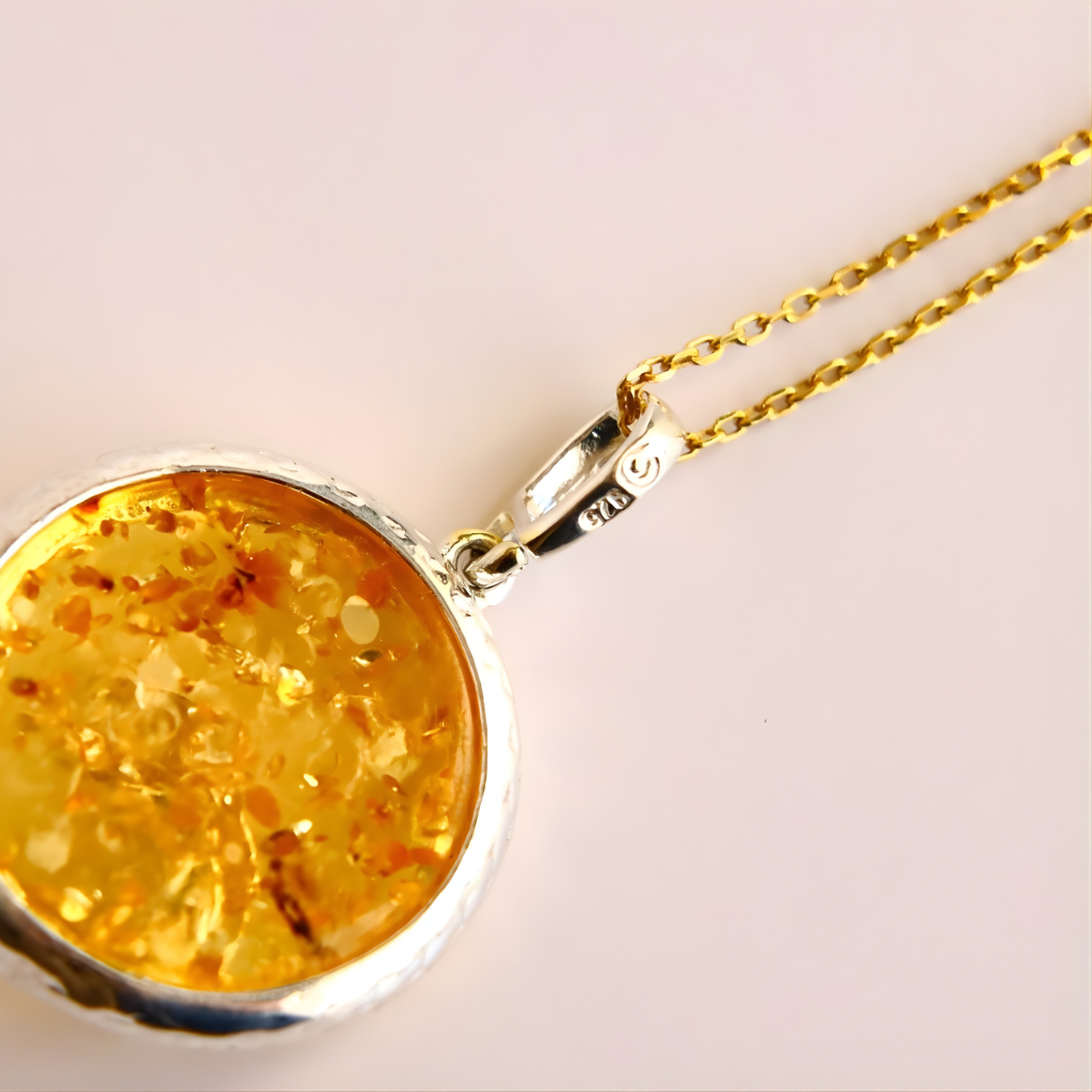 Gold amber necklace with a round pendant on a light pink background
