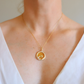 Gold amber necklace with a round pendant on a person wearing a white top.