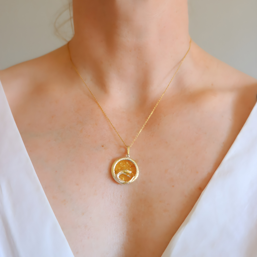 Gold amber necklace with a round pendant on a person wearing a white top.