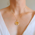 Gold amber necklace with a round pendant on a person wearing a white top.
