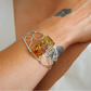 Silver cuff bracelet with a rectangular amber stone on a wrist.