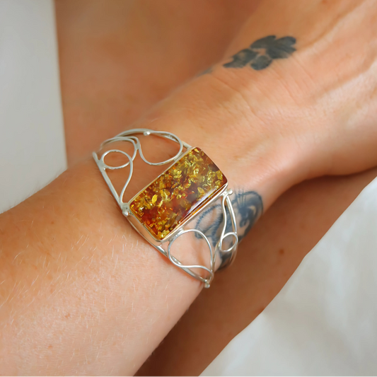 Silver cuff bracelet with a rectangular amber stone on a wrist.