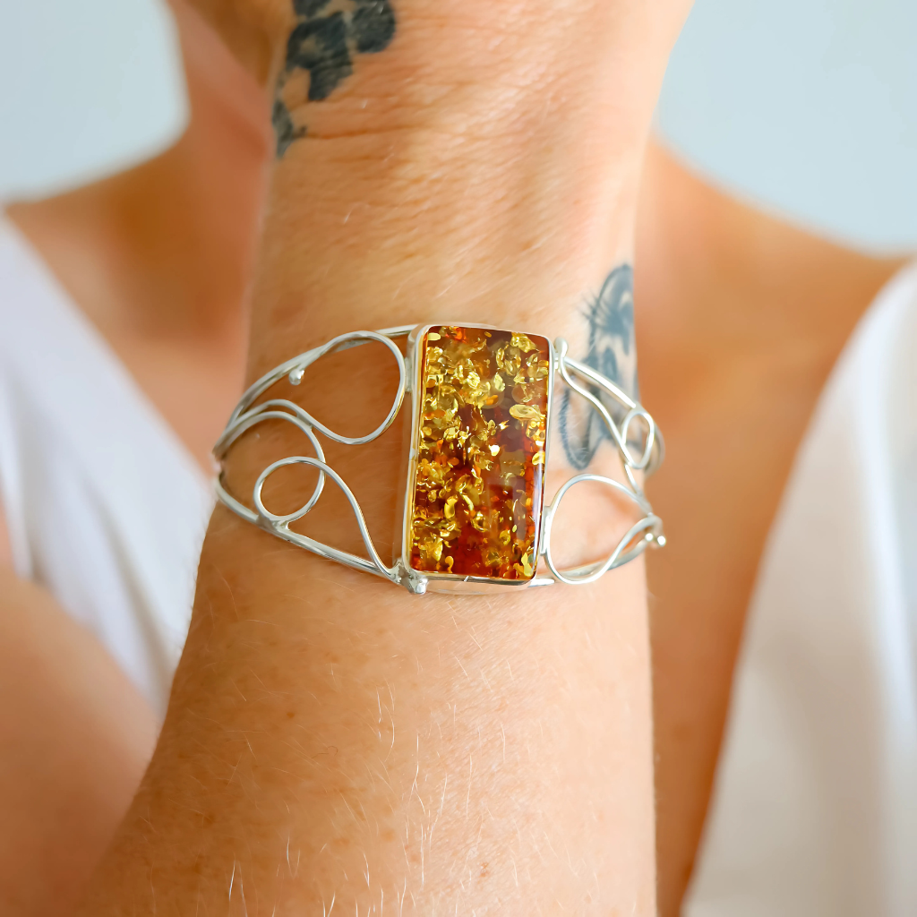 Silver cuff bracelet with amber stone on a wrist against a neutral background