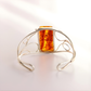 silver cuff bracelet with amber-colored stone on a light background