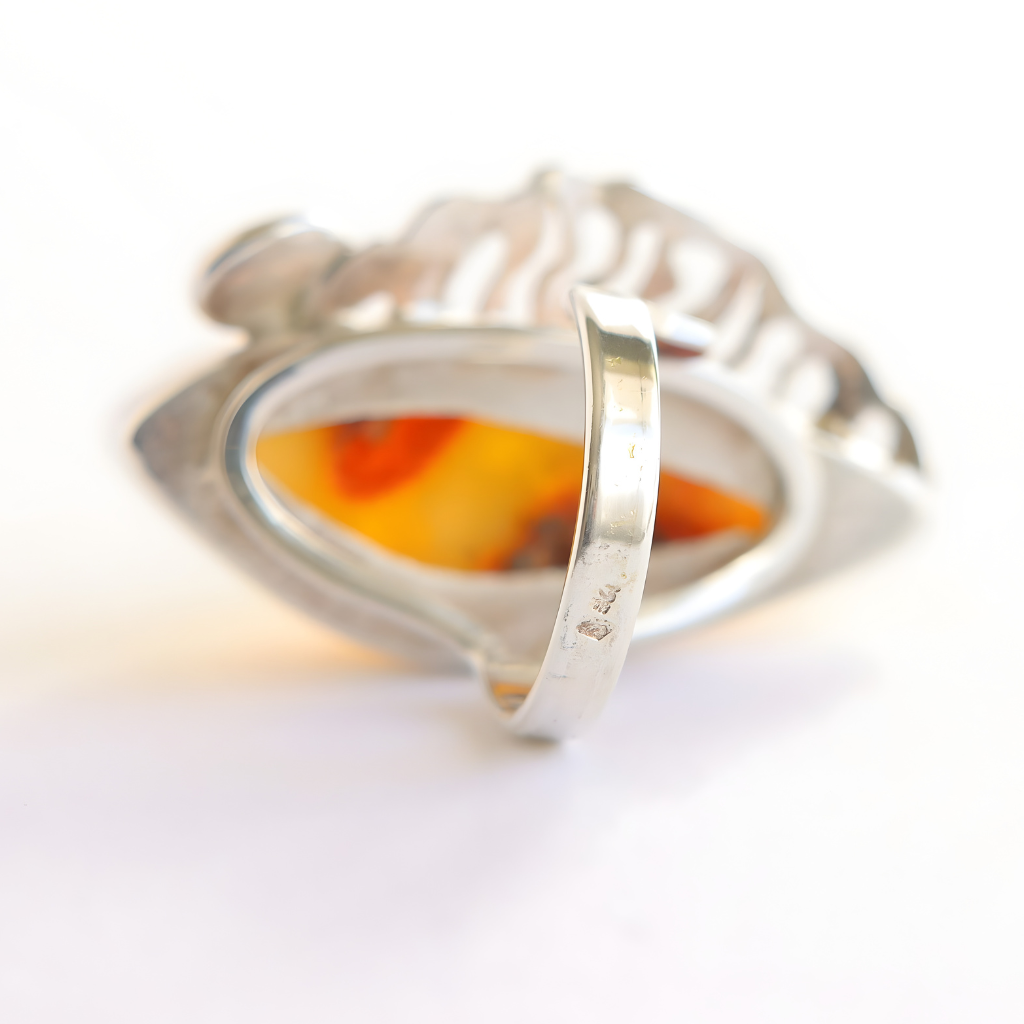 Silver butterscotch amber ring with a red and yellow stone on a white background