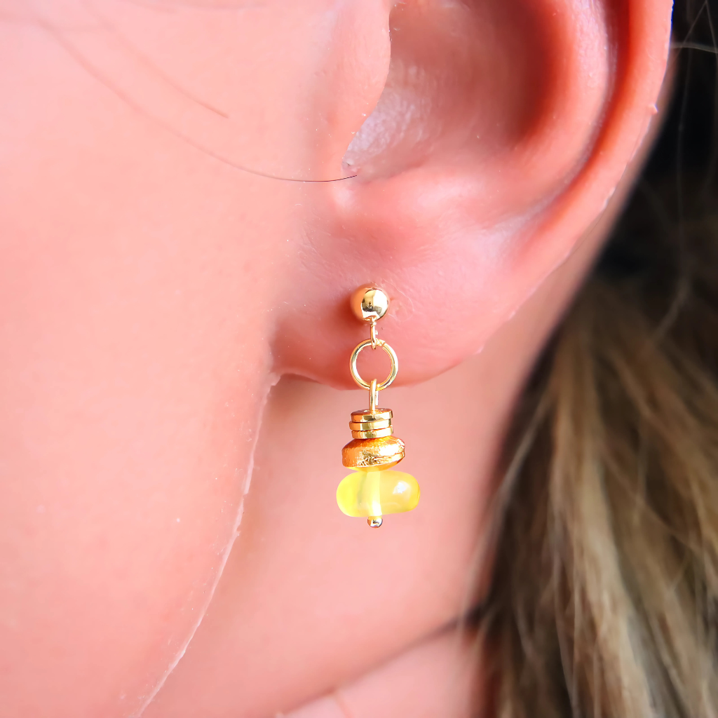 Handmade gold Baltic amber earrings worn on an ear, showcasing unique design and vibrant colors.