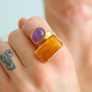Gold amber ring with purple and orange stones on a finger with a tattoo.