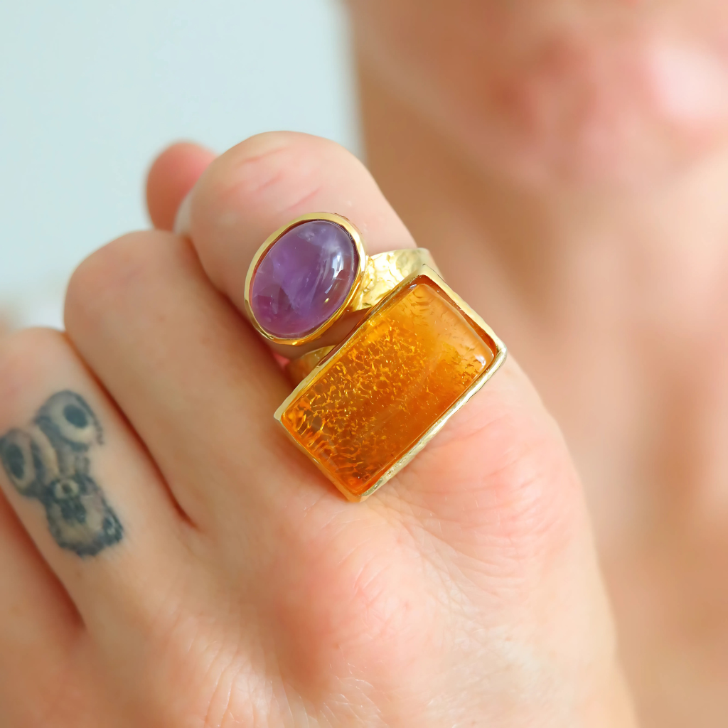Gold amber ring with purple and orange stones on a finger with a tattoo.