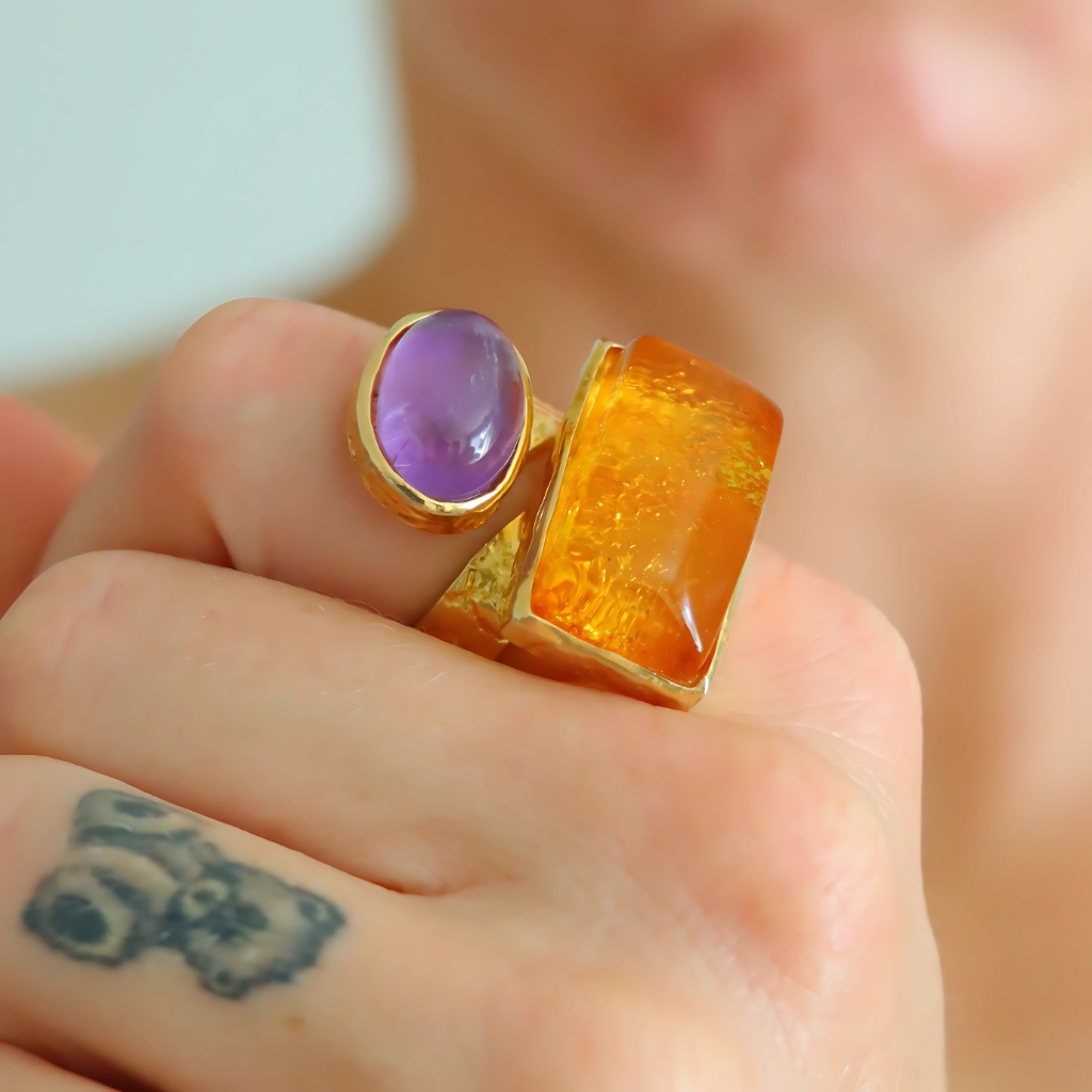 Close-up of a hand wearing an amber ring with purple and orange stones.
