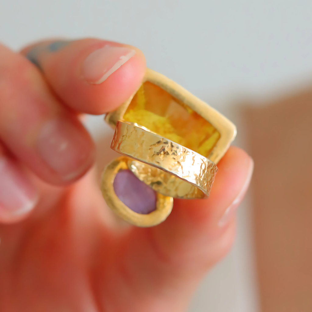 Gold amber ring with a yellow gemstone held in a hand against a neutral background