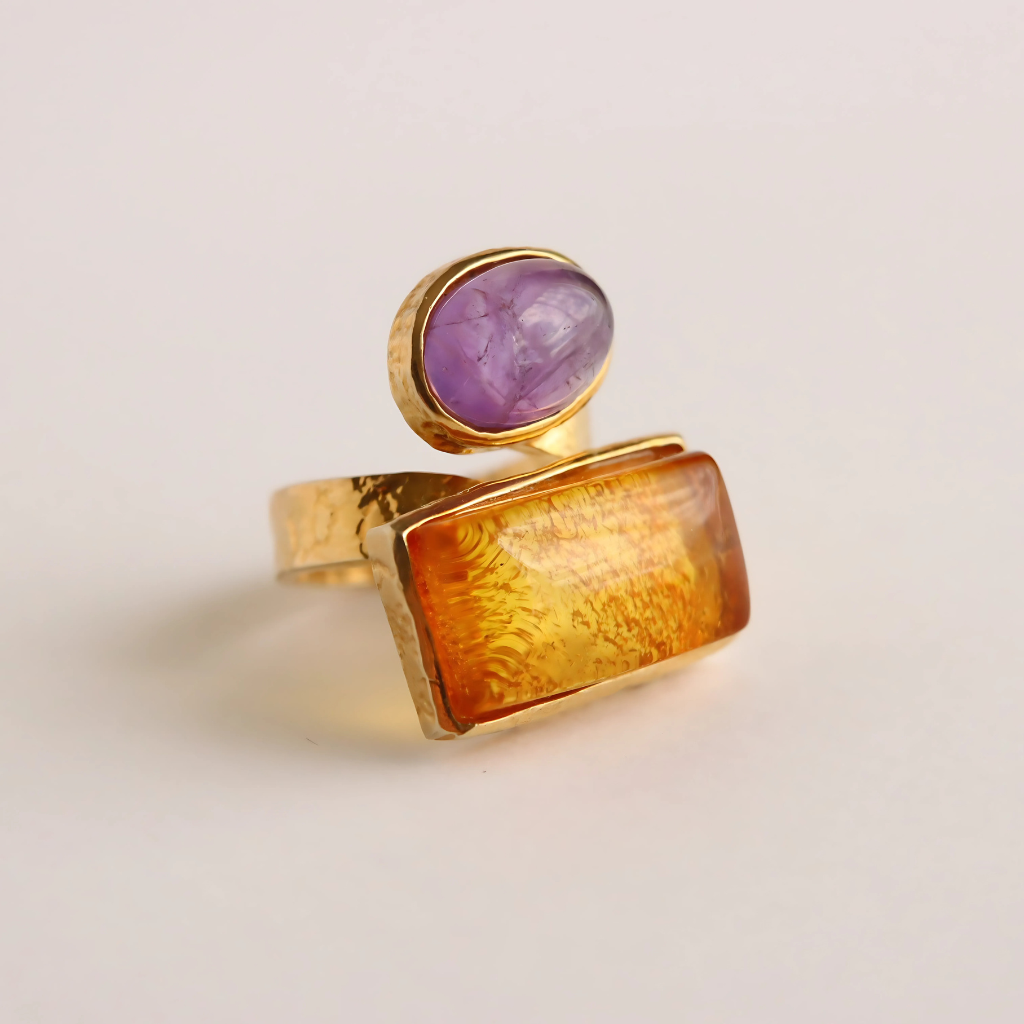 Gold amber ring with a purple gemstone on a light beige background