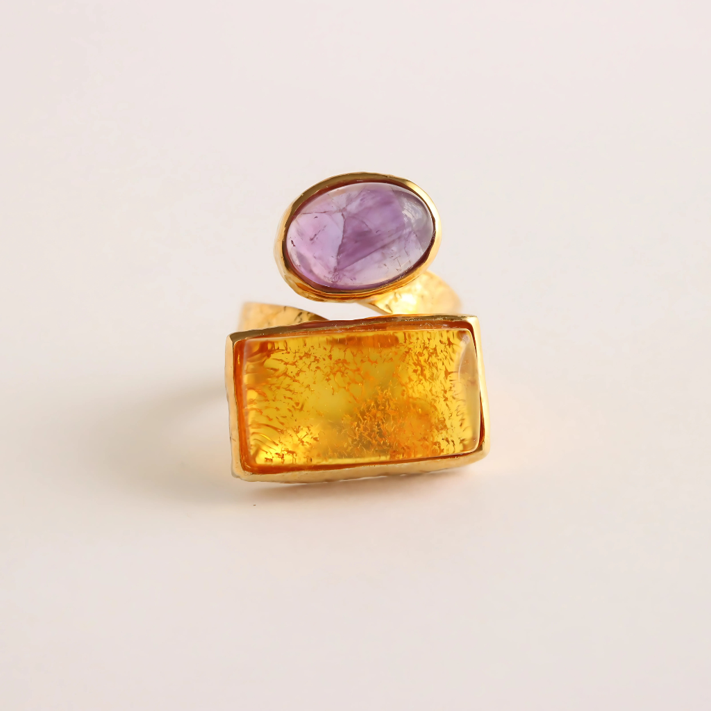 Gold amber ring with a purple gemstone on a light beige background