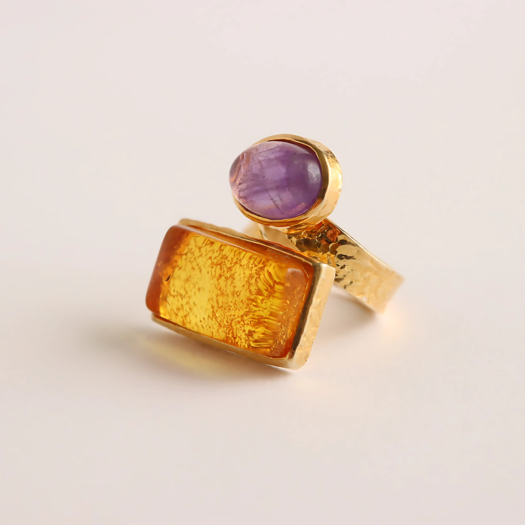 Gold amber ring with a purple gemstone on a light beige background
