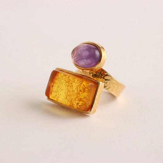 Gold amber ring with a purple gemstone on a light beige background