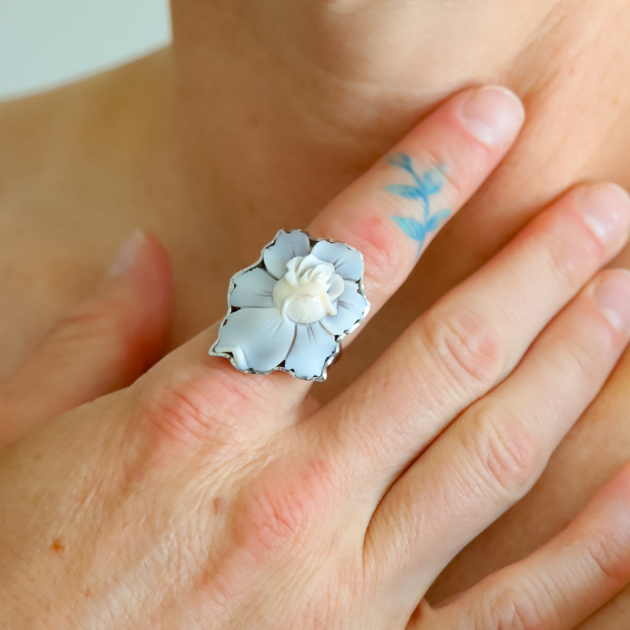 Hand wearing a blue flower ring with a rose blossom center