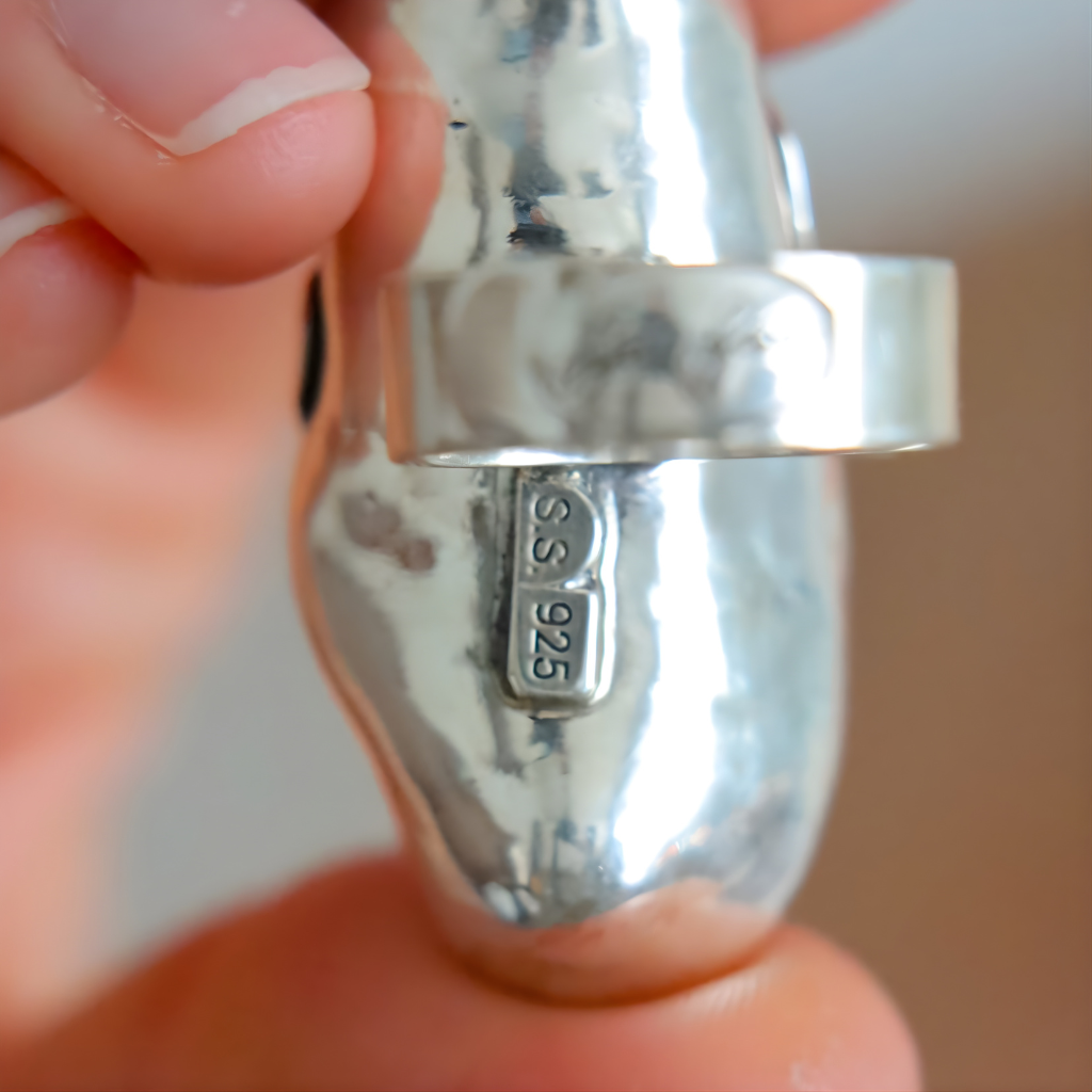 Close-up of a silver amber ring with 'S.S. 925' stamp held between fingers.