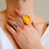 Hand wearing a yellow rose ring on a neutral background