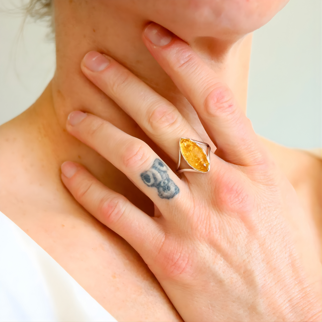 Close-up of a hand wearing a amber ring with a yellow gemstone, touching the neck.