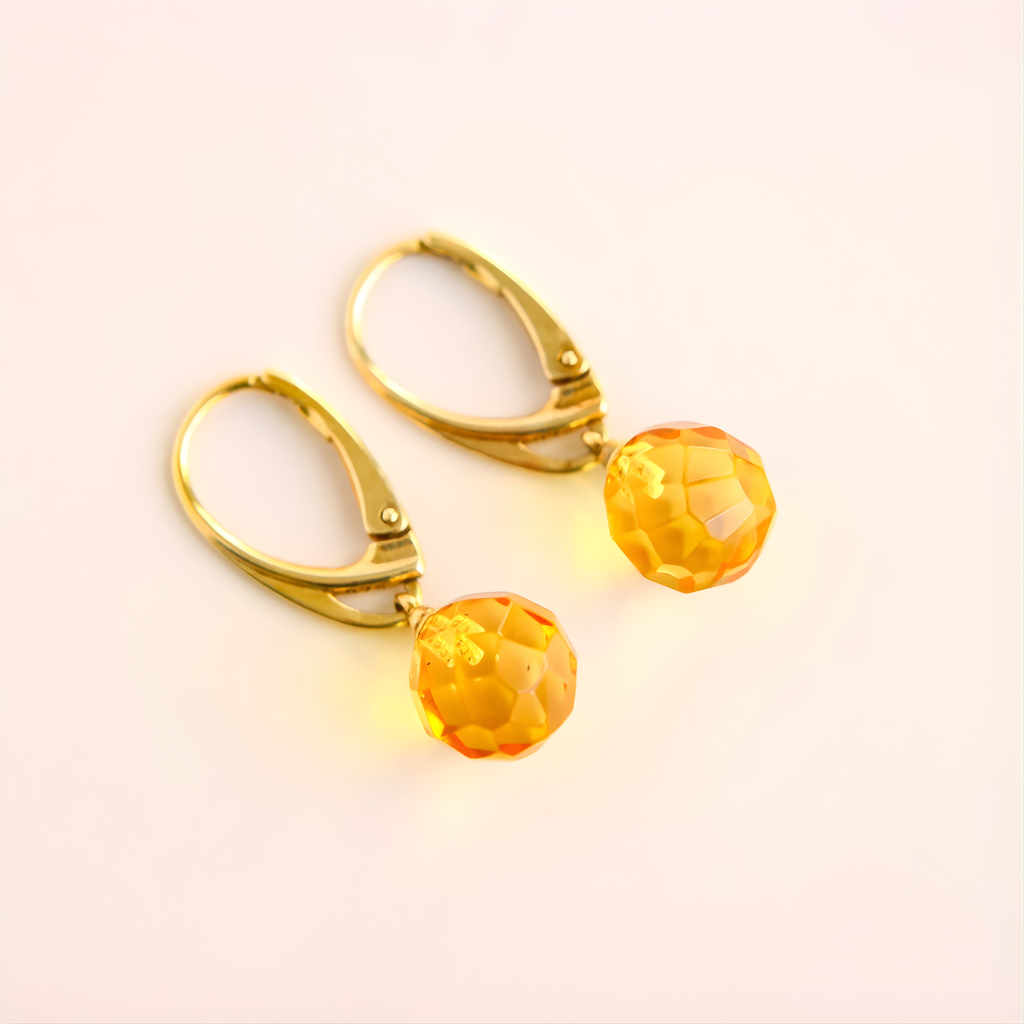 Gold amber earrings with orange gemstones on a light pink background