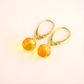 Gold amber earrings with orange gemstones on a light background